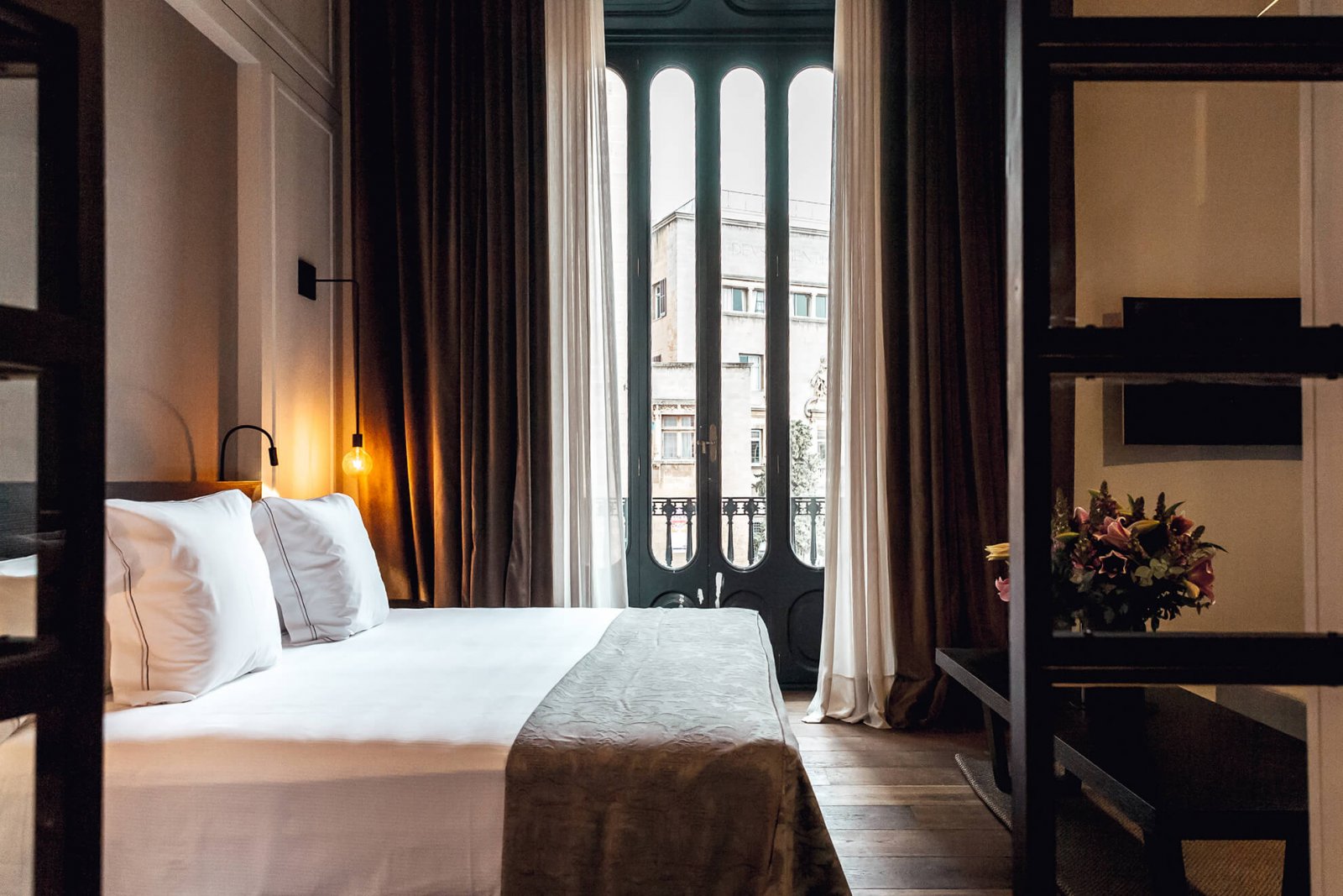 Another view of a room with a double bed, a balcony and details on the ceiling, a bookshelves and an area with a table and two armchairs