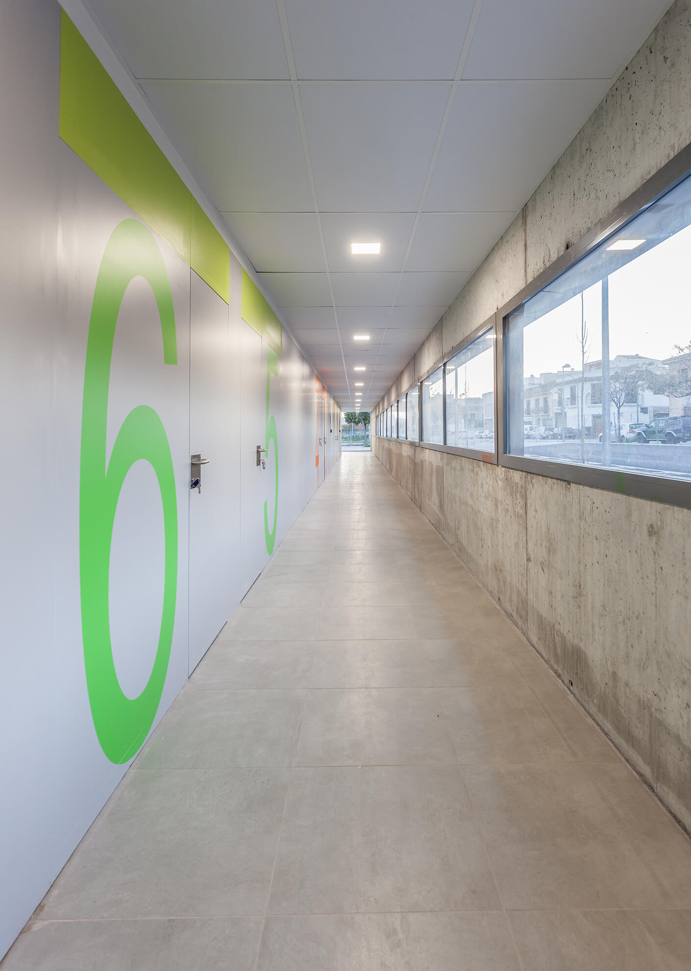 Detail view of the hallway of the pavilion with a concrete wall with windows to the outside, and doors dividing the different rooms