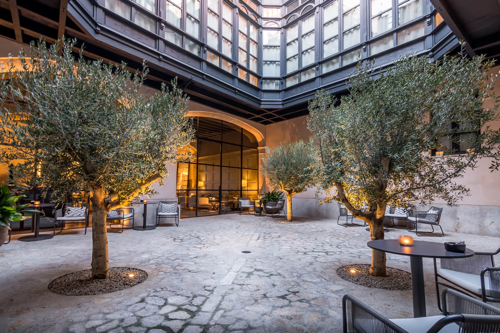 View of the interior patio with olive trees, stone floors and large windows with dark details